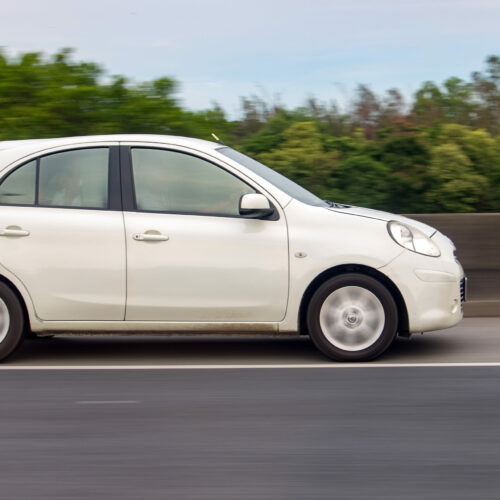 White car rides on highway with background blurred of motion.